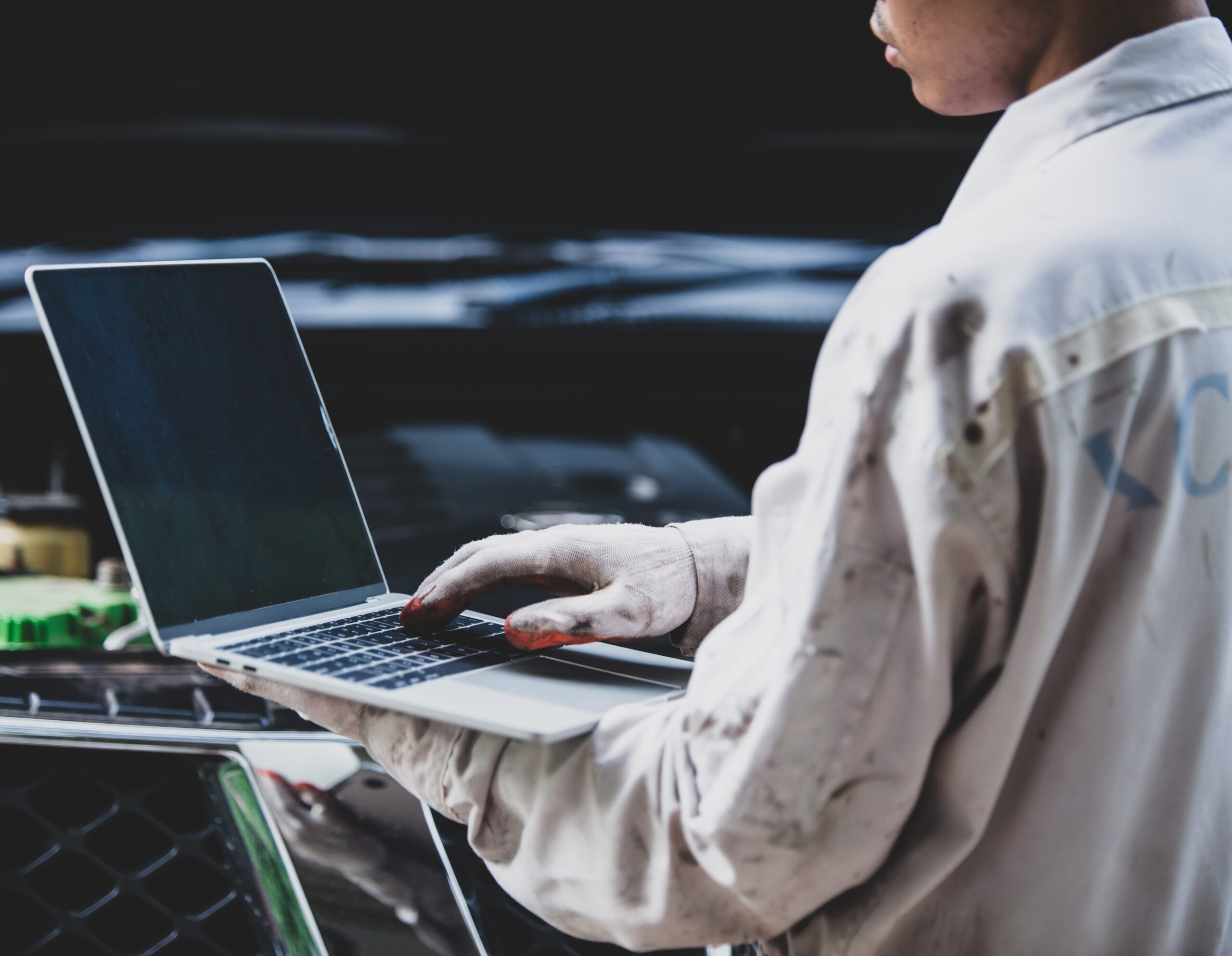 Car repairman wearing a white uniform standing and holding a wrench that is an essential tool for a mechanic with laptop checking engine
